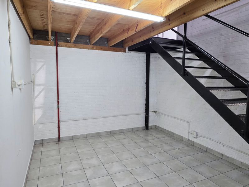 An industrial utility space featuring tiled flooring, painted brick walls, and a metal staircase leading to an exposed timber mezzanine level.