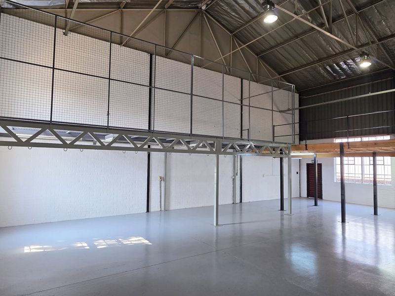 Spacious industrial warehouse unit featuring a high-clearance steel truss roof, mezzanine level, durable epoxy flooring, and secure roller shutter access.