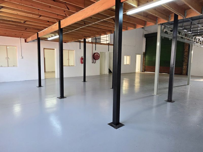 Spacious industrial utility area featuring exposed timber beams, steel support columns, polished epoxy flooring, and a large roller shutter door for easy access.