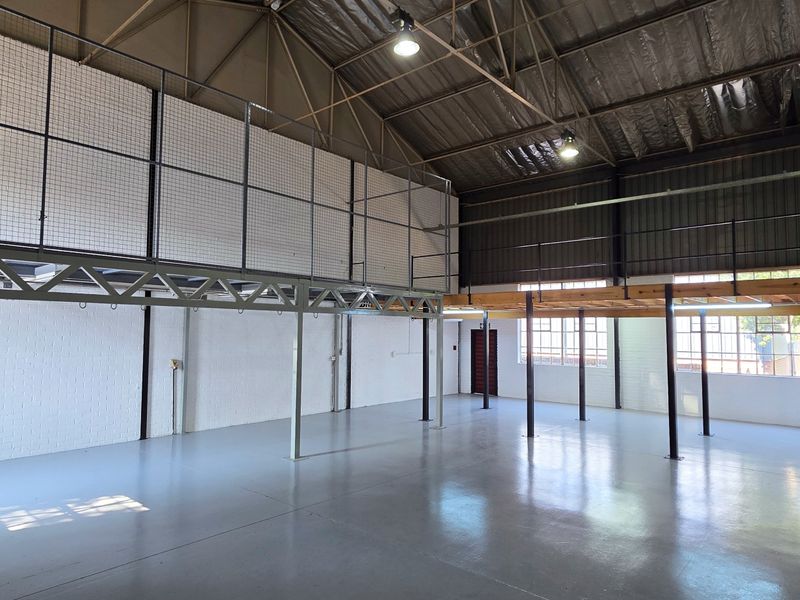 Spacious industrial warehouse unit featuring high ceilings with exposed trusses, a mezzanine level, durable epoxy flooring, and ample natural light through steel-framed windows.