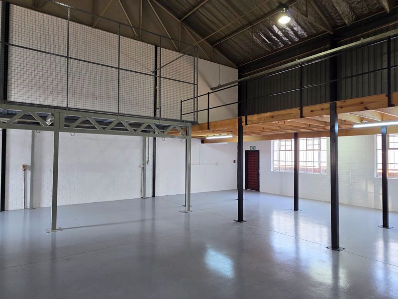 Spacious industrial open-plan warehouse area featuring a mezzanine level, steel support structures, polished epoxy flooring, and large steel-framed windows providing ample natural light.