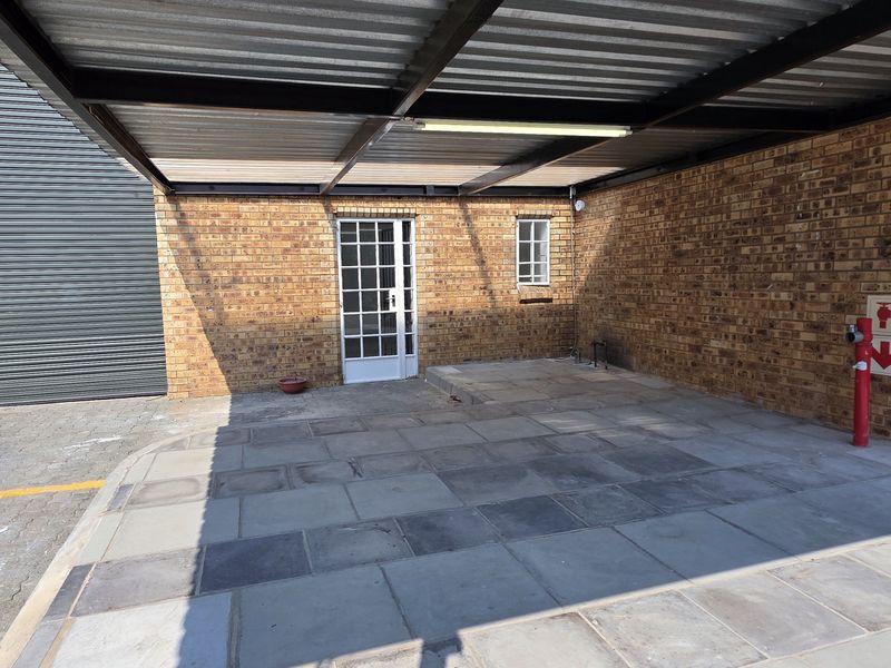 A covered industrial parking or loading area featuring facebrick walls, paved flooring, and a corrugated metal roof structure with a fire hydrant.