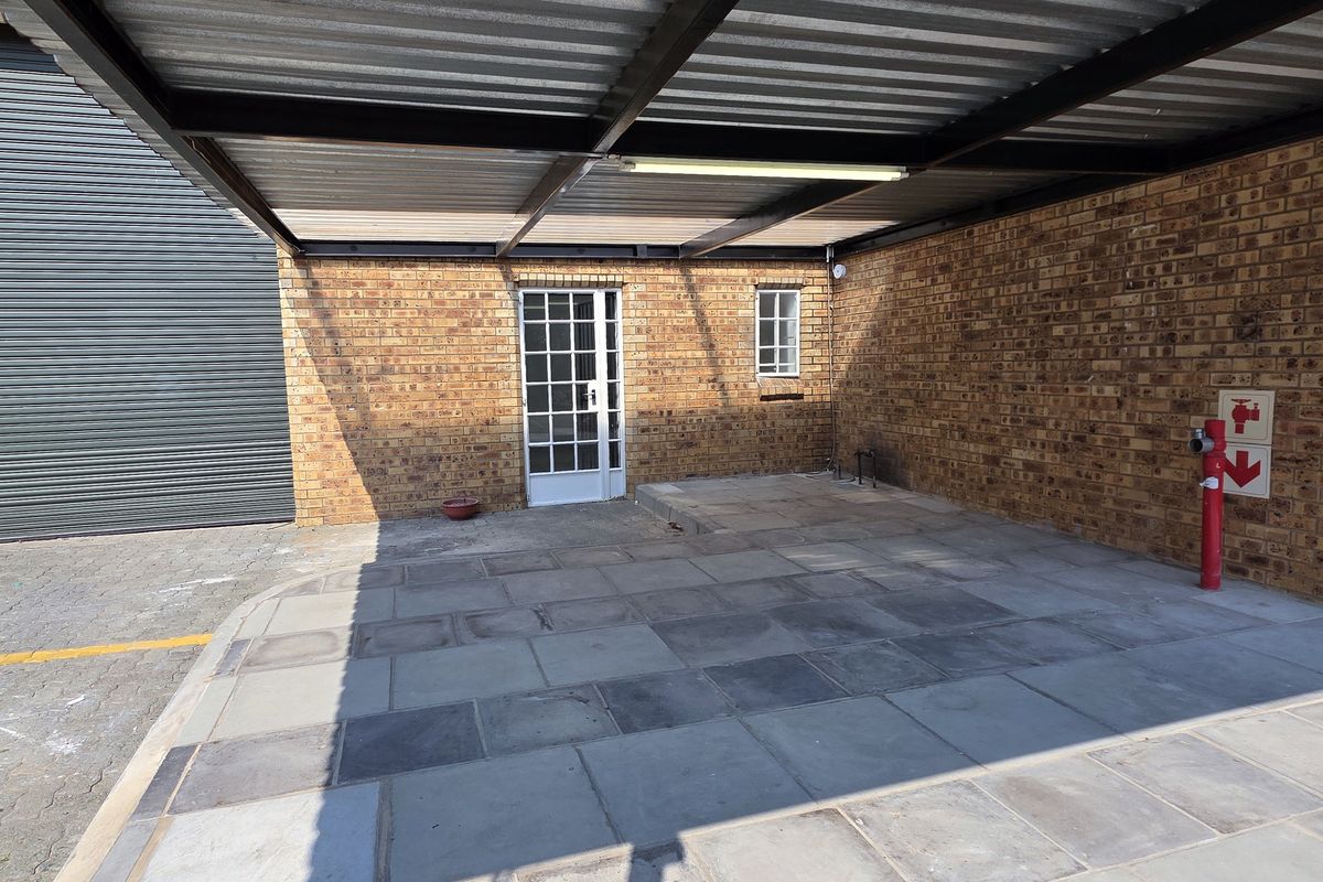 A covered industrial parking or loading area featuring facebrick walls, paved flooring, and a corrugated metal roof structure with a fire hydrant.
