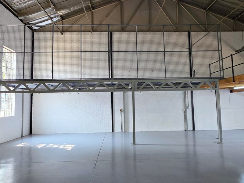 Spacious industrial warehouse unit featuring a mezzanine level, high exposed steel roof trusses, and durable epoxy-coated concrete flooring.