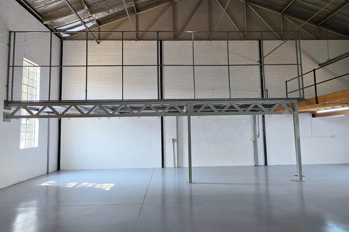 Spacious industrial warehouse unit featuring a mezzanine level, high exposed steel roof trusses, and durable epoxy-coated concrete flooring.