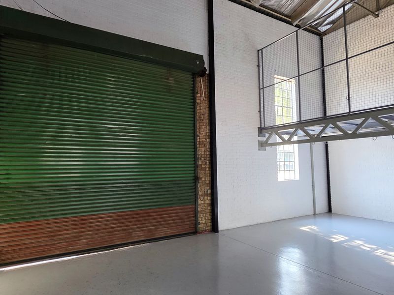 Spacious industrial utility area featuring a large roller shutter door, painted brick walls, epoxy flooring, and an elevated mezzanine level.