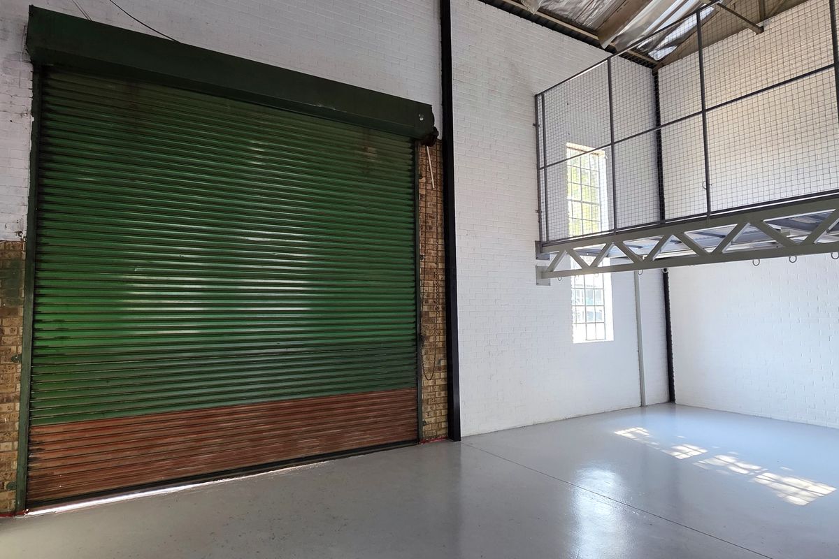 Spacious industrial utility area featuring a large roller shutter door, painted brick walls, epoxy flooring, and an elevated mezzanine level.