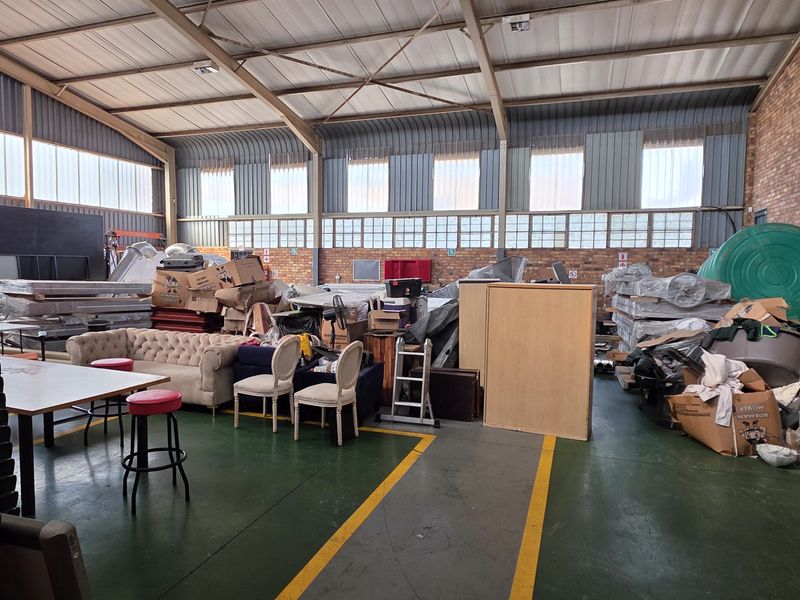 Spacious industrial utility area featuring high ceilings with exposed steel trusses, brick walls, and clerestory windows, suitable for storage or workshop operations.