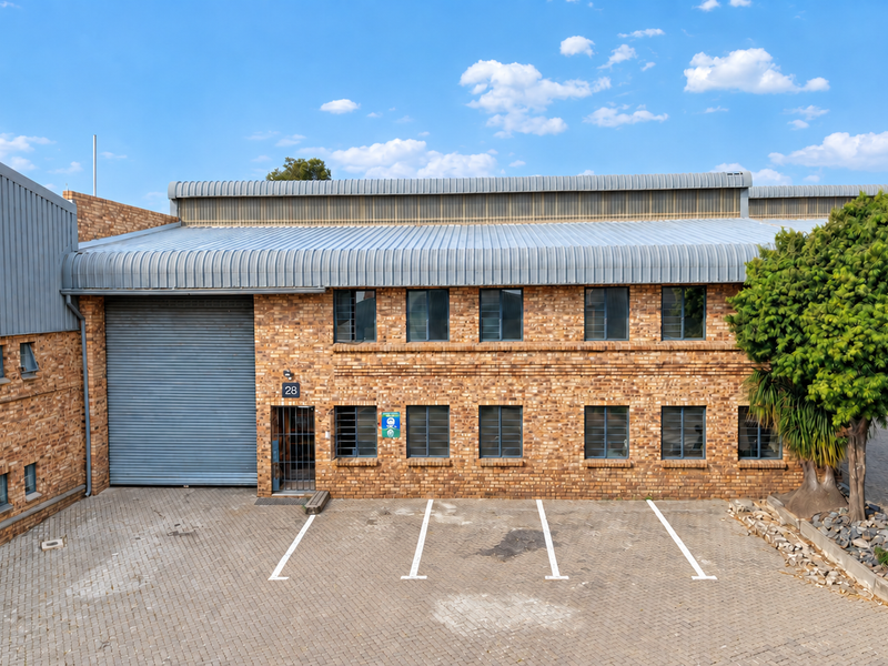Industrial unit featuring a face brick facade, large roller shutter door, and dedicated paved parking spaces in a well-maintained complex.