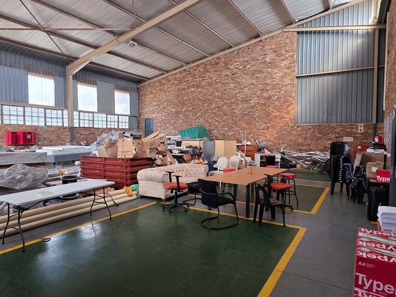 Spacious industrial utility area featuring exposed brick walls, high steel roof trusses, and durable painted concrete flooring with marked floor zones.