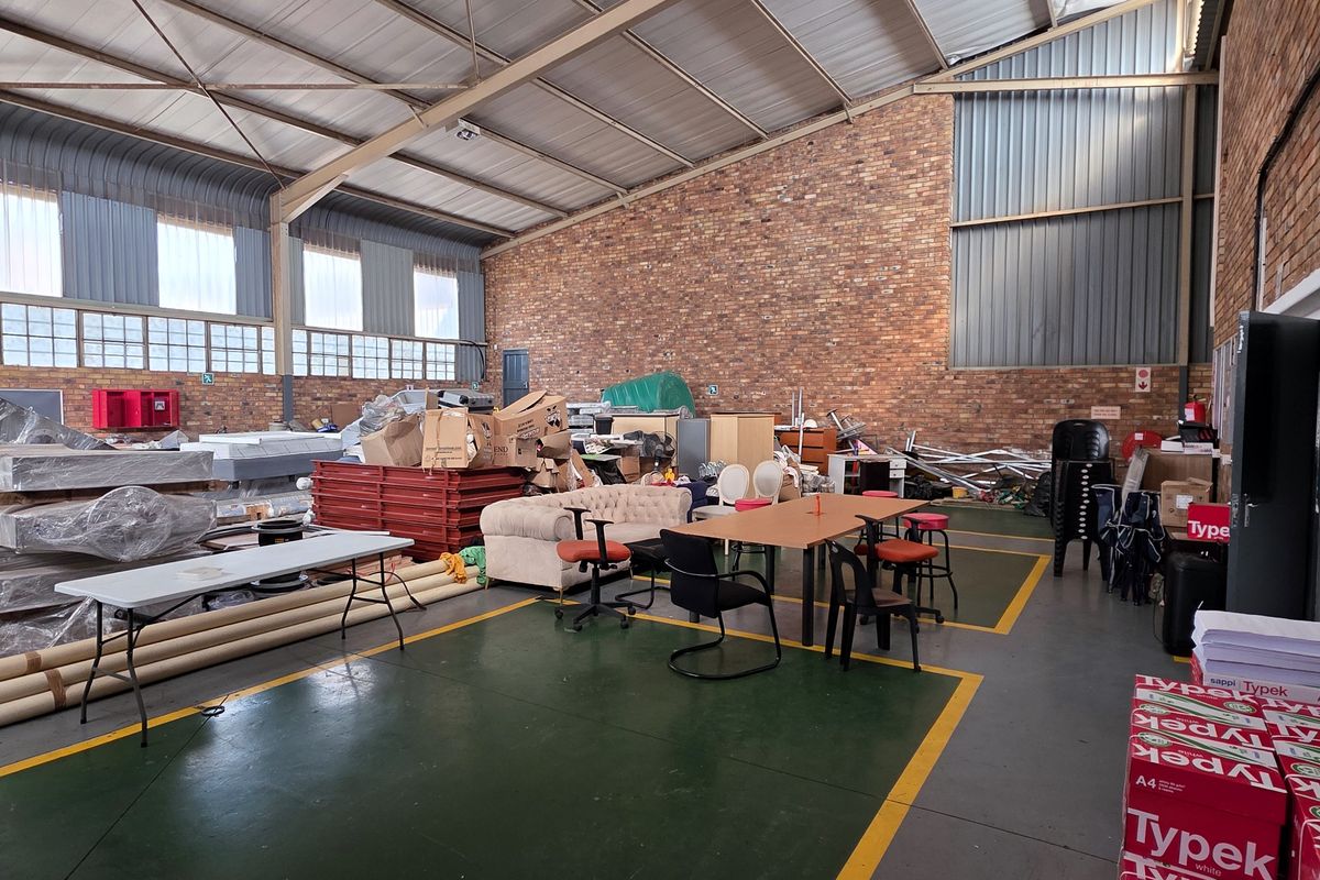 Spacious industrial utility area featuring exposed brick walls, high steel roof trusses, and durable painted concrete flooring with marked floor zones.