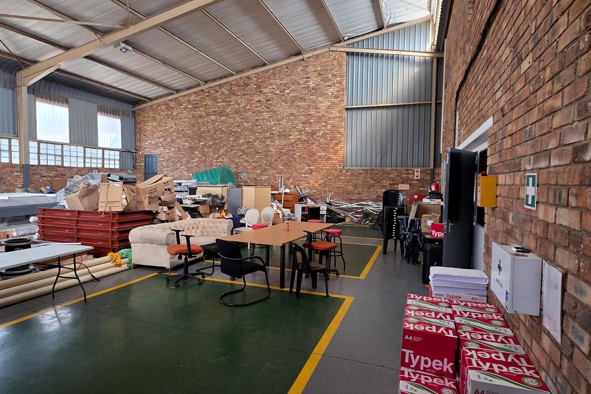 Spacious industrial utility area featuring exposed brick walls, high steel roof trusses, and durable painted concrete flooring with marked safety zones.