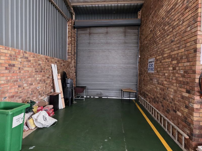Industrial utility space featuring exposed brick walls, a roller shutter door, and a painted concrete floor with safety markings.