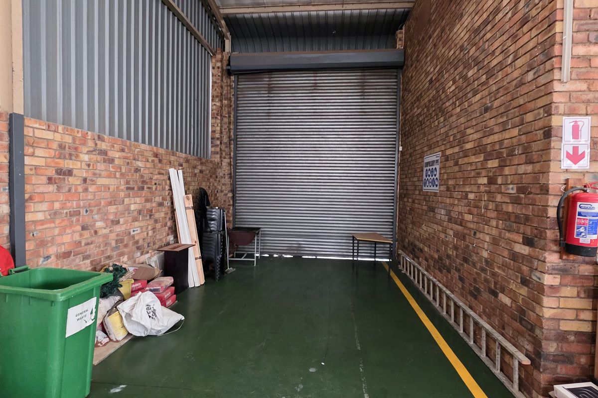 Industrial utility space featuring exposed brick walls, a roller shutter door, and a painted concrete floor with safety markings.