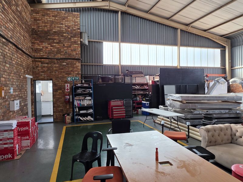 Spacious industrial warehouse area featuring exposed brick walls, high-pitched corrugated metal roofing, and durable epoxy-coated concrete flooring with ample natural light.