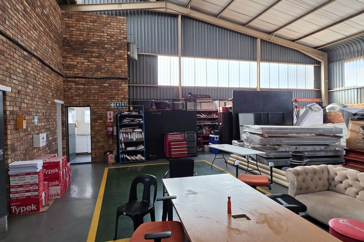 Spacious industrial warehouse area featuring exposed brick walls, high-pitched corrugated metal roofing, and durable epoxy-coated concrete flooring with ample natural light.