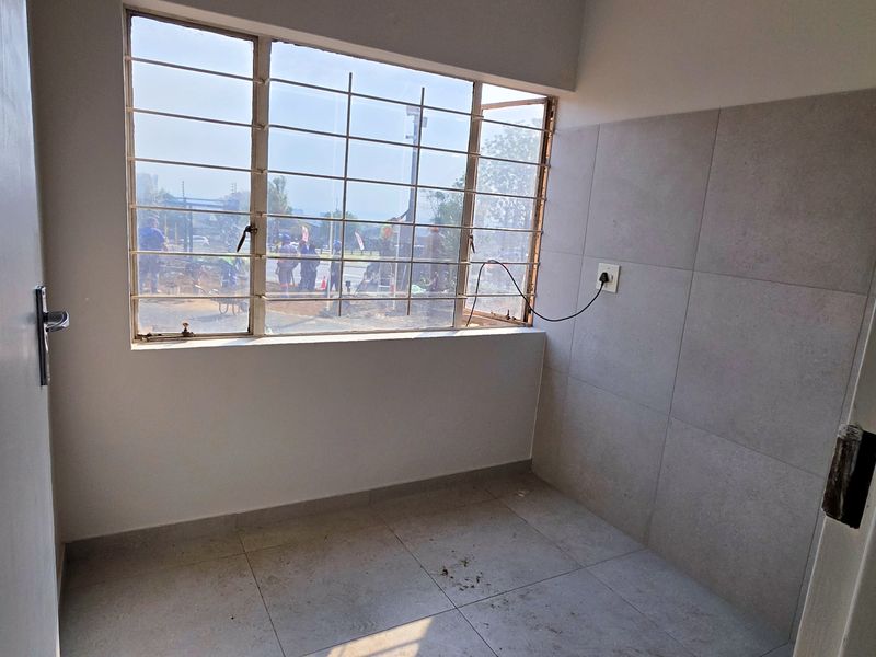 A compact, empty utility space featuring tiled flooring, wall tiling, and a window with security bars, suitable for laundry or storage use.