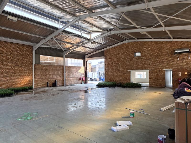 Spacious industrial warehouse unit featuring exposed brick walls, high steel truss ceilings with integrated skylights, and durable concrete flooring.
