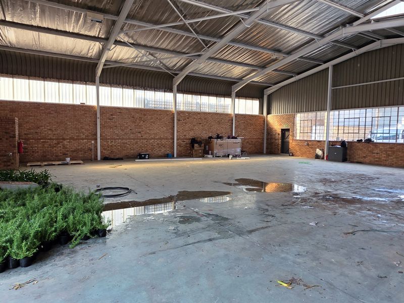 Spacious industrial warehouse unit featuring exposed brick walls, high-clearance steel portal frame roofing, and large steel-framed windows providing ample natural light.