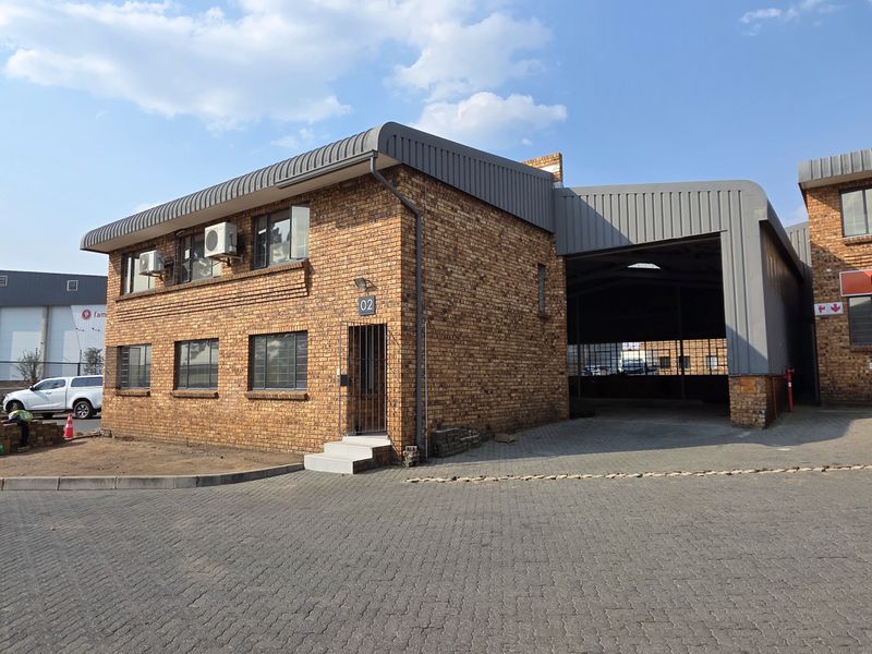 Front view of an industrial property featuring a face brick facade, paved driveway, and a covered loading bay area.