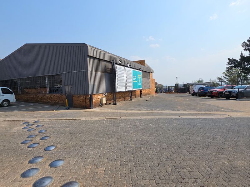 Exterior view of an industrial property featuring corrugated metal cladding, brick base, and a paved parking area with signage.