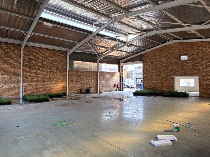 Spacious industrial warehouse unit featuring exposed brick walls, high steel truss ceilings with skylights, and durable concrete flooring, suitable for various commercial or storage uses.