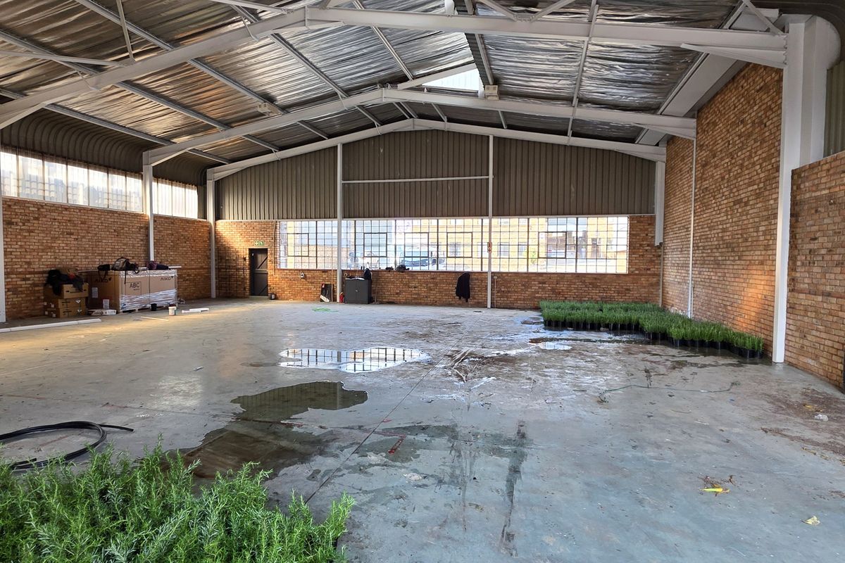 Spacious industrial warehouse unit featuring exposed brick walls, high steel-truss ceilings, and large industrial windows, offering a versatile open-plan layout.