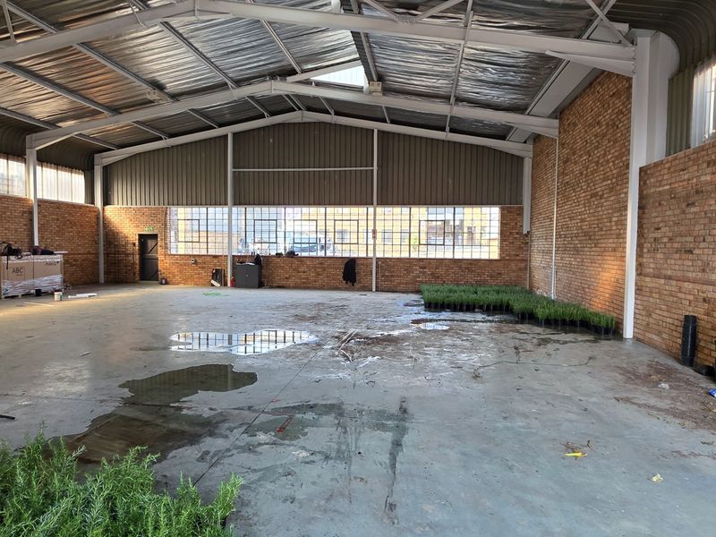 Spacious industrial warehouse unit featuring exposed brick walls, high steel portal frame ceilings, and large steel-framed windows, offering a versatile open-plan workspace.