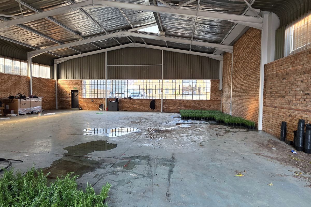 Spacious industrial warehouse unit featuring exposed brick walls, high steel portal frame ceilings, and large steel-framed windows, offering a versatile open-plan workspace.
