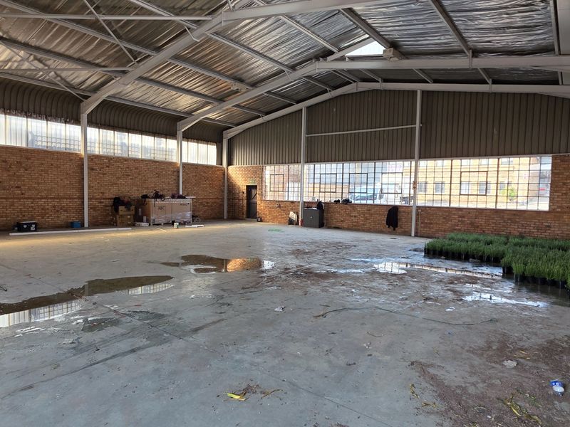 Spacious industrial warehouse unit featuring exposed brick walls, concrete flooring, and high-clearance steel truss roofing with natural light from steel-framed windows.