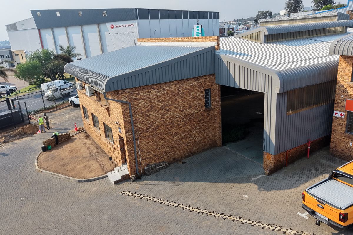 Aerial view of an industrial property featuring face brick construction, corrugated metal roofing, and a paved driveway with access to a large roller shutter door.