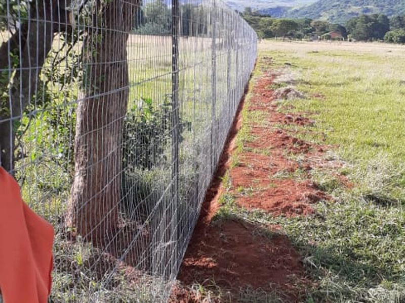 A view of the farm perimeter featuring newly installed wire mesh fencing and metal posts along the grassy field.
