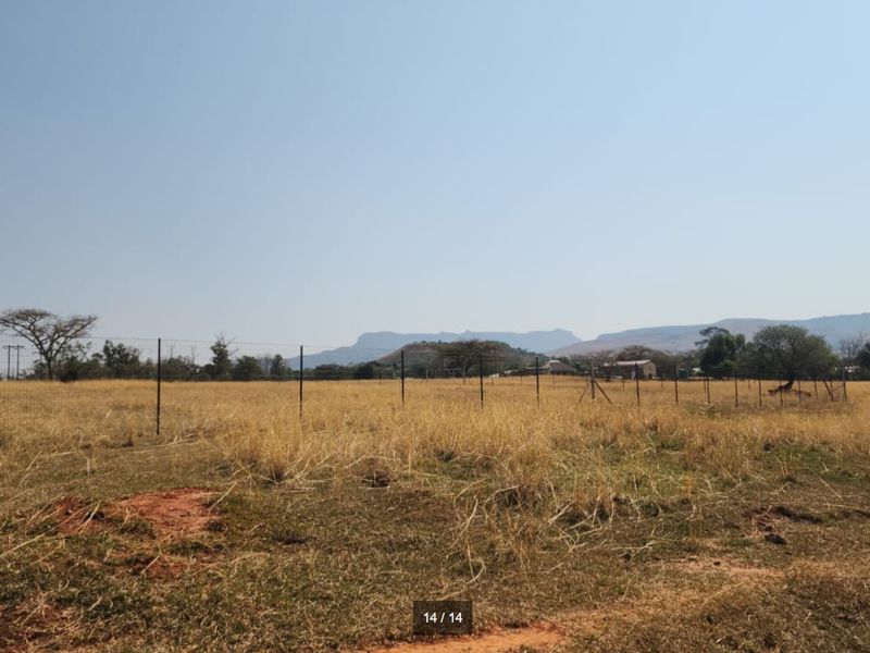 Expansive open farm land featuring wire fencing and scenic mountain views in the distance.