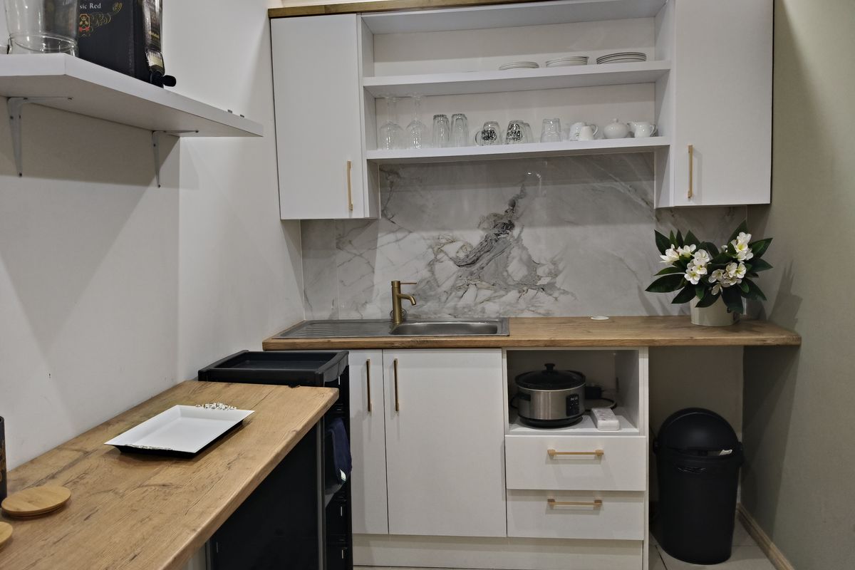 Compact kitchenette featuring white cabinetry, wood-look countertops, a marble-effect backsplash, and a stainless steel sink with modern brass fixtures.