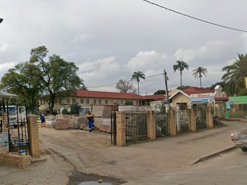 Street view of a commercial property site featuring a brick perimeter wall, metal security gate, and access to the main road.