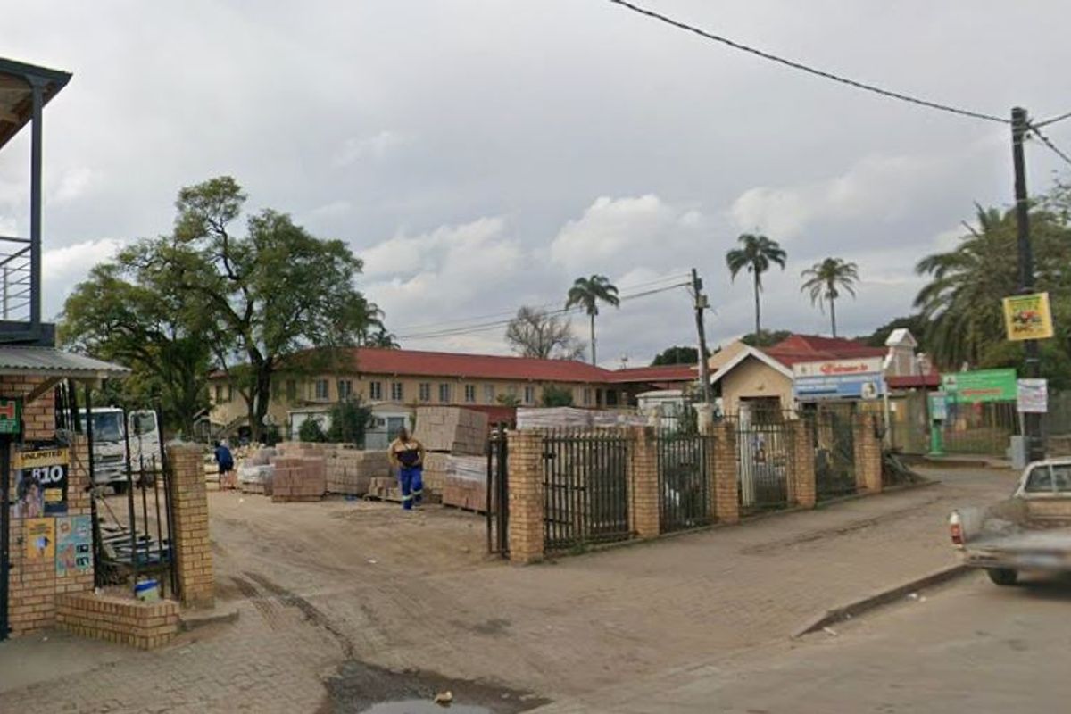 Street view of a commercial property site featuring a brick perimeter wall, metal security gate, and access to the main road.