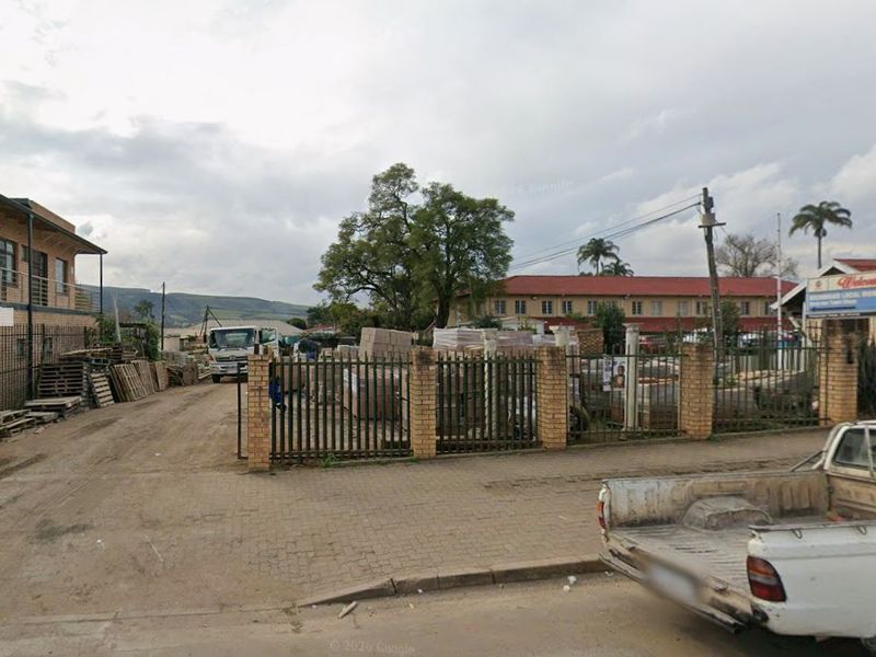 Street-level view of a commercial property featuring a paved driveway, brick perimeter wall, and metal security fencing.