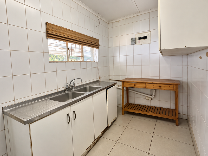 A functional scullery area featuring a stainless steel sink, tiled walls, and built-in cabinetry, requiring minor repairs and cosmetic updates.