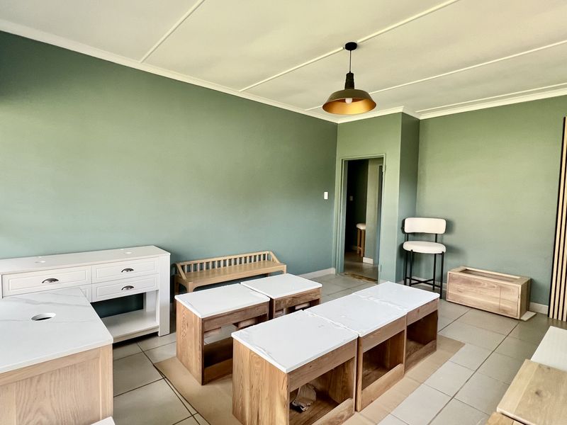 A bright, open office space featuring sage green walls, tiled flooring, modern pendant lighting, and decorative slatted wood wall paneling.