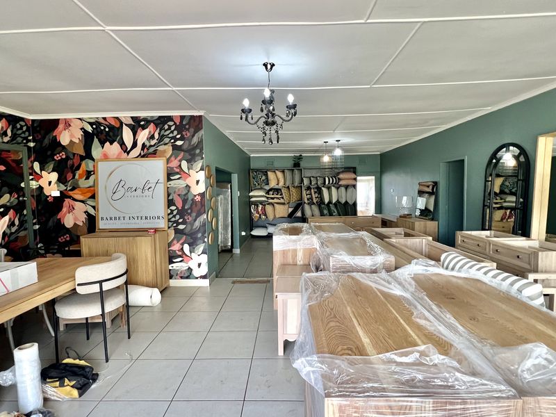 Spacious open-plan commercial showroom featuring tiled flooring, decorative floral wallpaper, and built-in shelving units, suitable for retail or display purposes.