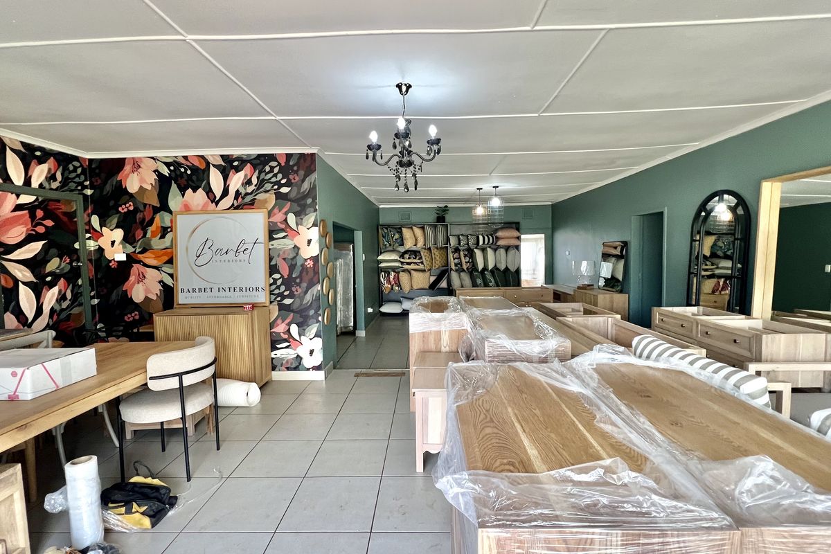 Spacious open-plan commercial showroom featuring tiled flooring, decorative floral wallpaper, and built-in shelving units, suitable for retail or display purposes.