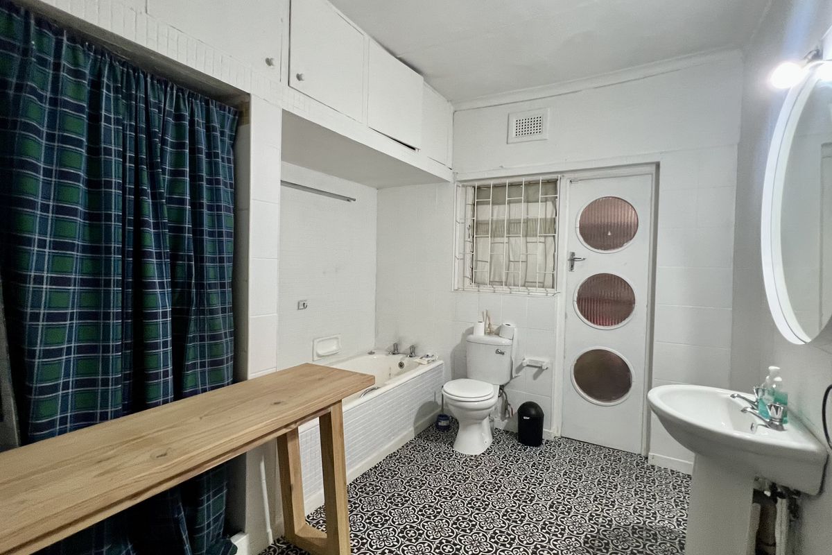 A functional bathroom featuring a built-in bathtub, pedestal sink, toilet, and overhead storage cabinetry with patterned floor tiles.