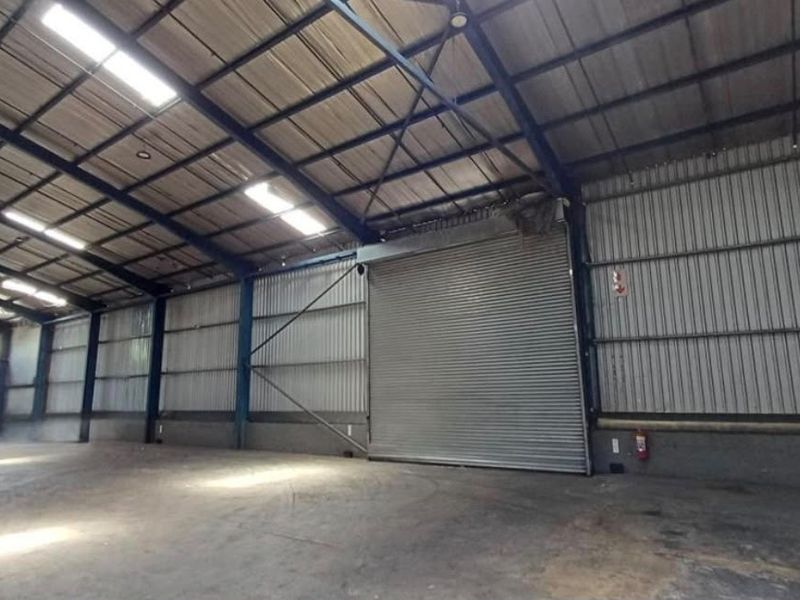 Spacious industrial warehouse unit featuring high ceilings, concrete flooring, natural light through skylights, and a large roller shutter door for easy access.