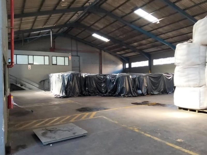 Spacious industrial warehouse area featuring high ceilings with exposed steel trusses, skylights, and durable concrete flooring suitable for storage or manufacturing operations.