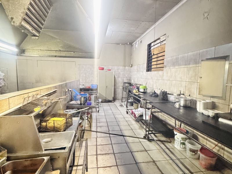 Commercial kitchen facility featuring stainless steel prep counters, industrial extractor hood, and tiled flooring, suitable for high-volume food preparation.