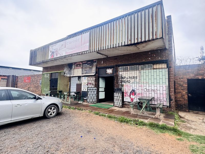Commercial storefront featuring brick facade, metal signage, security gates, and gravel parking area, suitable for retail or food service business.