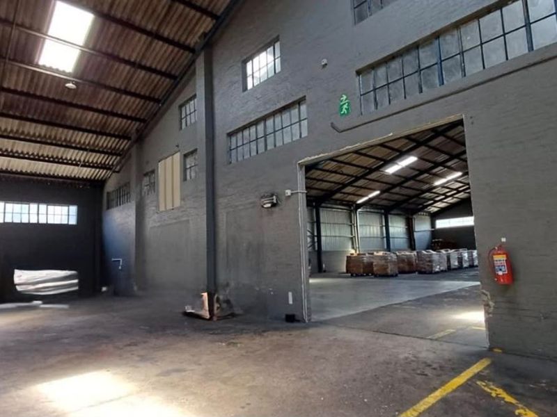Spacious industrial warehouse unit featuring high ceilings with exposed steel trusses, concrete flooring, and large steel-framed windows providing natural light.