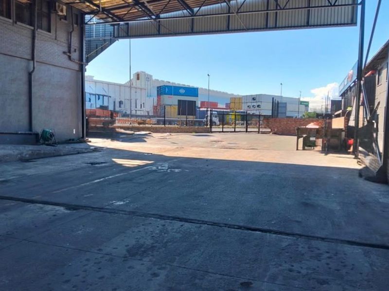 A large industrial utility space featuring a concrete floor and overhead steel roof structure, providing open access to the exterior yard area.