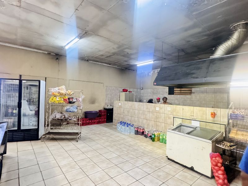 Commercial kitchen area featuring tiled flooring, a large extractor hood, and tiled service counter, requiring significant maintenance and cosmetic updates.