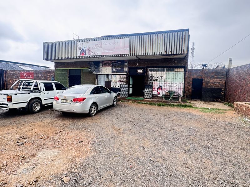 Commercial property exterior featuring a brick facade, metal cladding, and an unpaved gravel parking area, suitable for retail or business use.